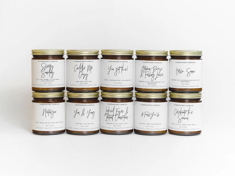 Ten candles in jars with white labels and black text stacked in two rows
