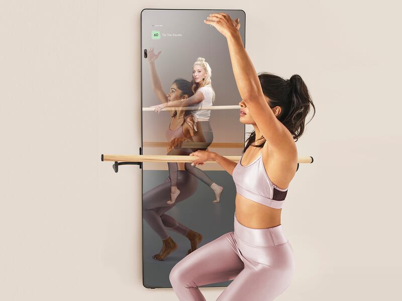 A woman practices barre exercises in front of a smart mirror
