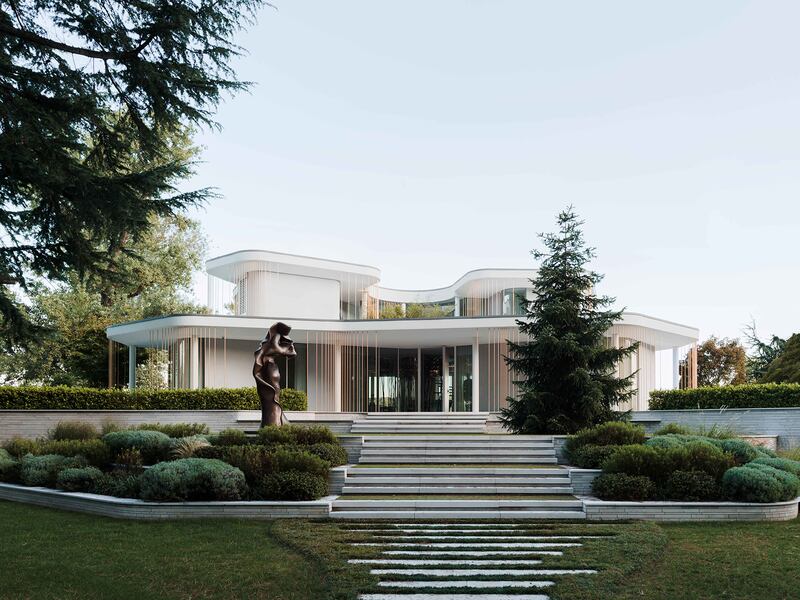 Large, white modern villa surrounded by trees and a lawn