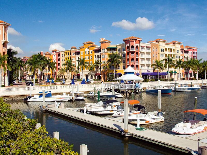 Yellow, pink and white condos line the edge of a harbor, with four white boats moored to a jetty.
