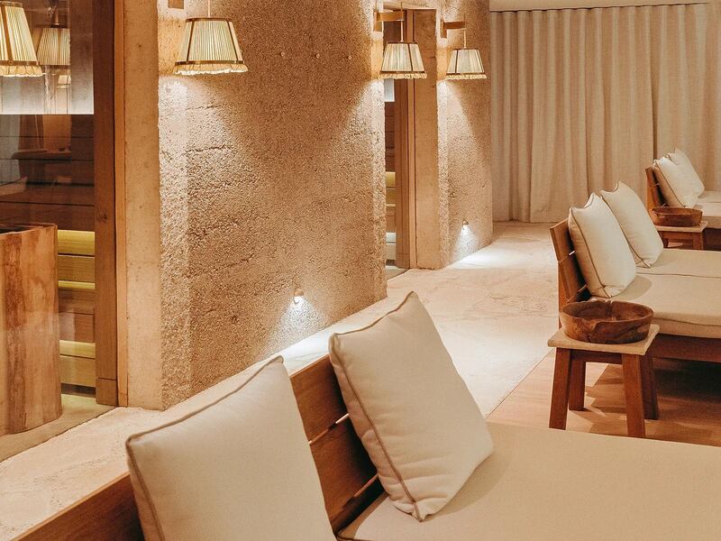 A sandy colored treatment room with rustic walls and wooden daybeds with cream colored cushions