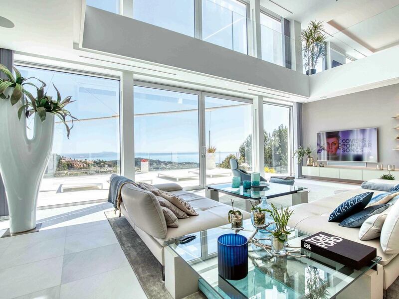 A bright sitting room with two sofas facing a TV has double-height walls of glass looking out over unoccupied Spanish countryside.