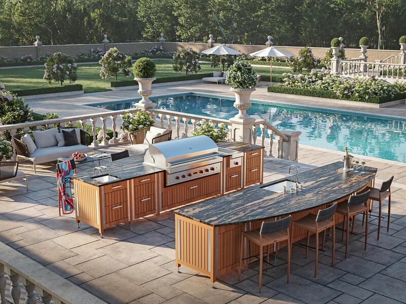 A wooden outdoor kitchen and an island with bar seating on a terrace next to a pool in the formal garden of a stately home.