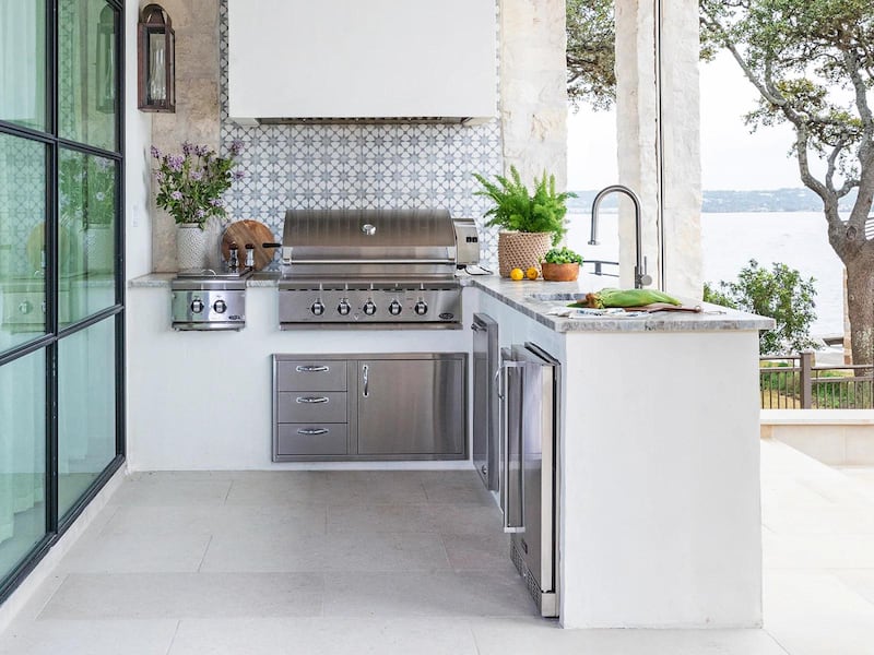 A sleek, white outdoor kitchen with vases of flowers and potted plants on the work surfaces.