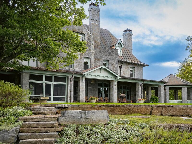 Stone steps in a green, terraced garden lead up to a large stone house in Ferrisburgh, Vermont, with porches and two tall chimneys.