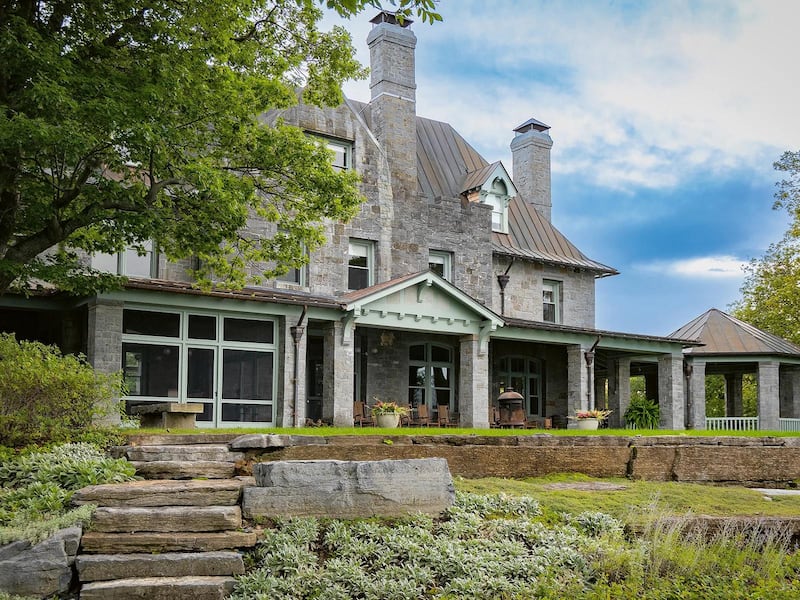 Stone steps in a green, terraced garden lead up to a large stone house in Ferrisburgh, Vermont, with porches and two tall chimneys.