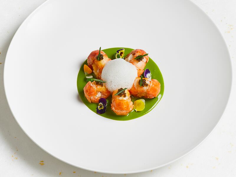 A gourmet dish of lobster tails and foam served on a green sauce