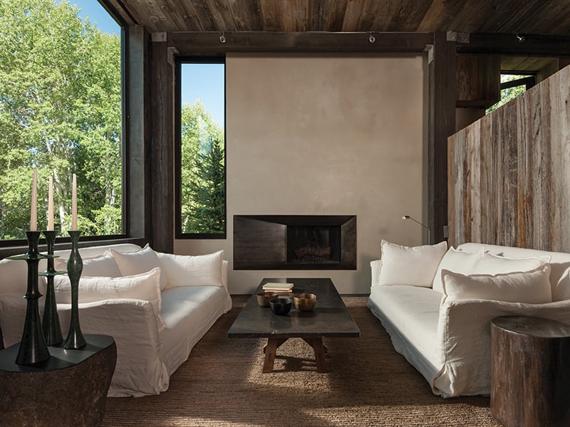A living room with white sofas, large garden-facing windows, and reclaimed wood walls